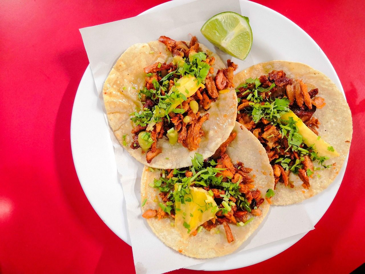 Three crispy tacos with meat, cilantro, onion, lime wedge on white plate